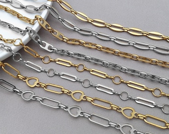 Könnte beinhalten: Eine Auswahl an gold- und silberfarbenen Kettenhalsketten. Die Ketten weisen verschiedene Gliederdesigns auf, darunter ovale, rechteckige und herzförmige Glieder. Die Halsketten werden auf einer hellgrauen Oberfläche präsentiert, wobei einige Ketten teilweise auf einem weißen Teller liegen.