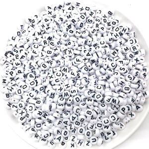 May include: A white bowl filled with white plastic alphabet beads. The beads have black letters on them.