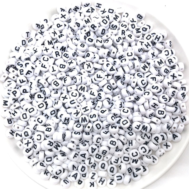 May include: A white bowl filled with white plastic alphabet beads. The beads have black letters on them.