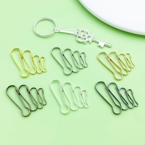 May include: A selection of metal keyrings and clasps in gold, silver, and black. The keyrings have a decorative key design. The clasps come in three sizes. The items are displayed on a green surface.