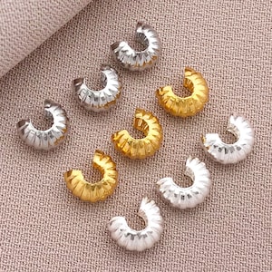 Peut inclure: Un assortiment de composants de bijoux en forme de croissant, de couleur argent et or. Les composants ont une texture striée et sont disposés sur une surface texturée brun-rosé. Ces composants sont parfaits pour créer des boucles d'oreilles, des bracelets ou des colliers.