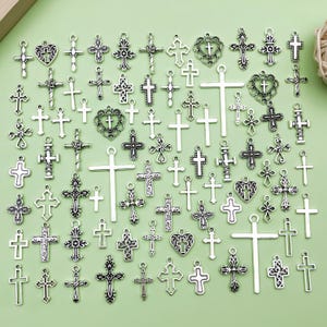 May include: A collection of silver-colored cross charms in various sizes and designs. Some crosses feature ornate detailing, while others have a simple, classic appearance. Several heart-shaped charms with crosses are also present.