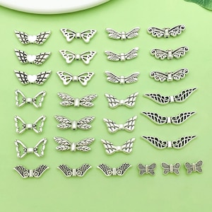 May include: A collection of silver-colored butterfly-shaped charms in various designs, including bowties and wing shapes. The charms are arranged on a light green surface, showcasing their intricate details and textures. Ideal for jewelry making or craft projects.