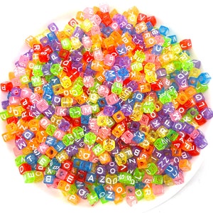May include: A large pile of colorful, translucent alphabet letter beads. The beads are square shaped and have white letters on them.