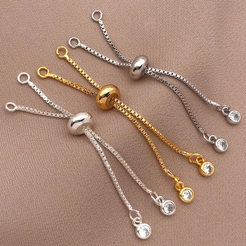 K&ouml;nnte beinhalten: Vier verstellbare Kettenarmb&auml;nder in Silber und Gold mit klaren Kristallperlen. Die Armb&auml;nder haben einen Schiebeverschluss, um die L&auml;nge anzupassen.