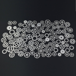 May include: A collection of silver metal gears of various sizes and shapes, arranged in a random pattern on a black background.