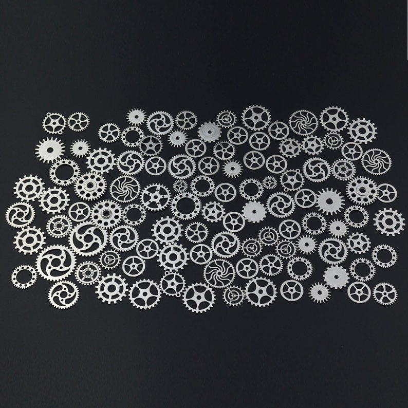 May include: A collection of silver metal gears of various sizes and shapes, arranged in a random pattern on a black background.