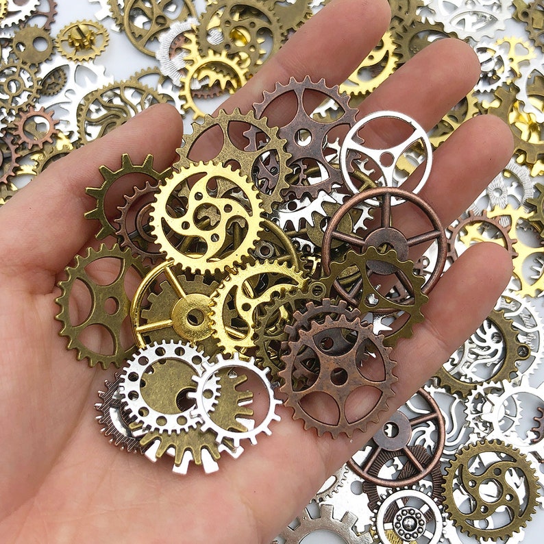 May include: A collection of antique gold and silver gears and cogs, some with intricate designs, arranged in a hand. The gears are various sizes and shapes, with some having a more rustic look.