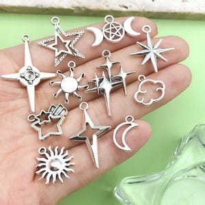 K&ouml;nnte beinhalten: Eine Sammlung silberfarbener Anh&auml;nger in verschiedenen Himmelsformen. Die Anh&auml;nger umfassen Sterne, Monde, Sonnen und Wolken. Jeder Anh&auml;nger hat eine kleine Schlaufe zum Befestigen an Schmuck oder anderen Bastelarbeiten. Die Anh&auml;nger werden vor einem hellgr&uuml;nen Hintergrund pr&auml;sentiert.