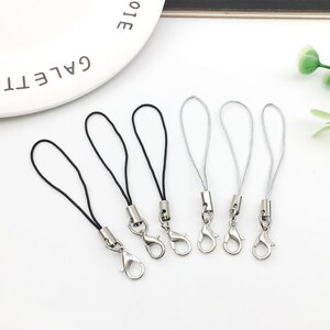 Op de afbeelding: Zes zilveren sleutelhangers met zwarte en zilveren koorden. De sleutelhangers hebben een zilveren karabijnhaak.