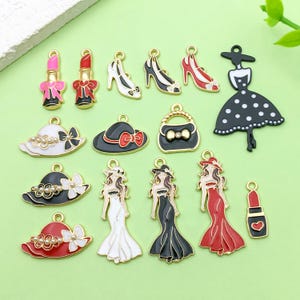 Könnte beinhalten: Eine Sammlung von Mode-Charms in verschiedenen Designs. Enthält Lippenstifte, High Heels, Hüte, Handtaschen und Kleider-förmige Charms. Die Charms sind in Gold, Schwarz, Weiß und Rot gehalten. Ideal für die Schmuckherstellung oder Bastelarbeiten.
