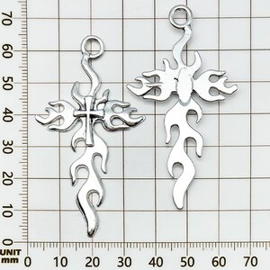 May include: Two silver-colored cross pendants with a flame design. Each cross has a loop at the top for hanging and measures approximately 2.5 inches in length. The crosses are displayed against a grid background.