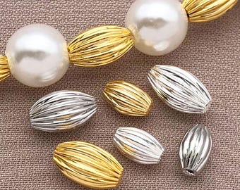 May include: A close-up of a variety of gold and silver beads. The beads are oval shaped and have a ribbed texture. The beads are arranged in a row on a brown surface.