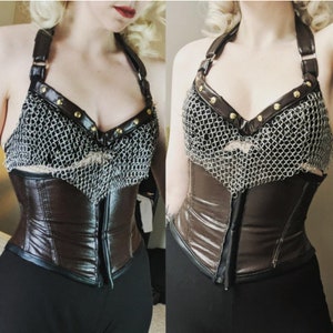May include: A brown leather corset with a chainmail top. The corset has a zipper in the back and is cinched at the waist. The chainmail top has gold accents.