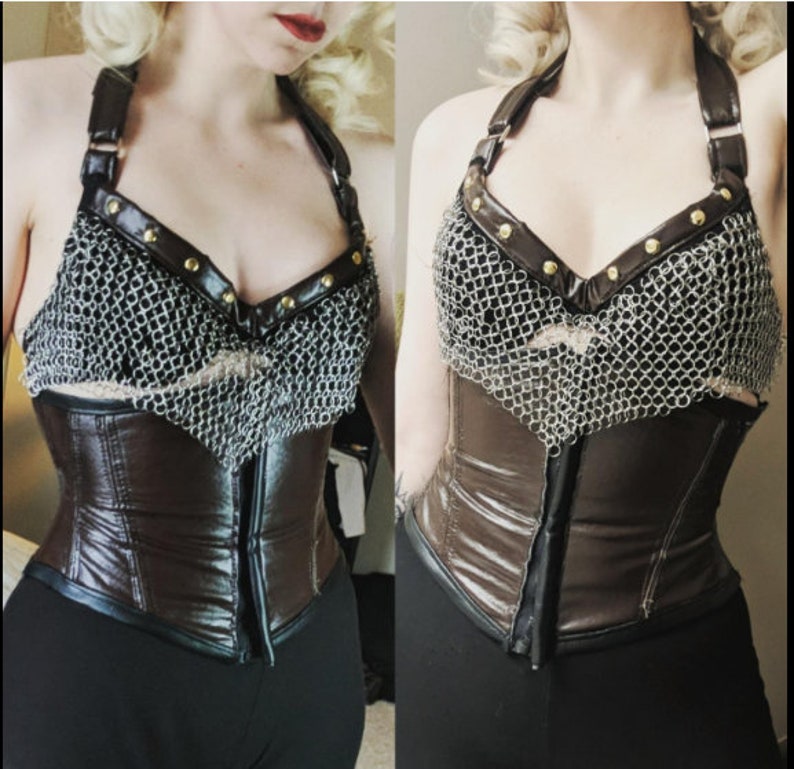 May include: A brown leather corset with a chainmail top. The corset has a zipper in the back and is cinched at the waist. The chainmail top has gold accents.