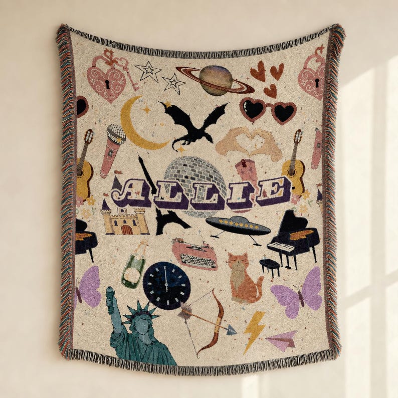 May include: A woven throw blanket featuring a cream background with the name ALLIE in purple letters. The design includes a dragon, disco ball, planet, guitar, piano, typewriter, Statue of Liberty, cat, butterflies, hearts, and various other icons.