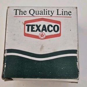 May include: A vintage box with the Texaco logo in red and white, featuring a red star. The box has the words "The Quality Line" printed at the top. A green wavy design is at the bottom.