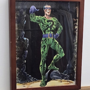 Könnte beinhalten: Gerahmte Comic-Kunst mit dem Riddler, einem DC Comics-Superschurken. Der Riddler ist in einem grünen Anzug mit Fragezeichen, einer lila Maske und Handschuhen dargestellt. Das Kunstwerk ist in einem braunen Holzrahmen gerahmt.