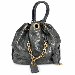 May include: A dark gray bucket bag featuring a textured snakeskin pattern, a single top handle, and gold-tone metal hardware. The bag includes a drawstring closure with large gold grommets and a decorative gold chain accent with a matching leather tag.