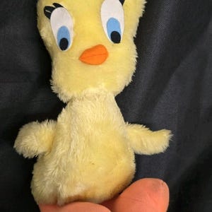 May include: A plush yellow Tweety Bird toy with a sad expression. The toy has large blue eyes, an orange beak, and orange feet. The plush toy is a classic cartoon character.