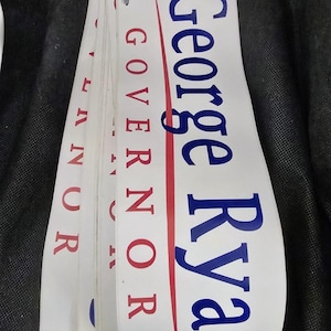May include: A stack of white political campaign stickers. The stickers have the name "George Ryan" in blue, and the word "GOVERNOR" in red. A red vertical line runs through the middle of the stickers.