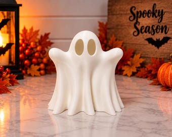 Puede incluir: Una figura blanca y hueca con forma de fantasma y dos aberturas ovaladas para los ojos. El fantasma tiene un aspecto liso, fluido y drapeado con una cabeza redondeada y brazos extendidos, de pie como un objeto decorativo de temporada.