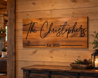 Puede incluir: Un letrero rectangular de madera con un acabado de veta natural y letras negras que dicen The Christophers y Est 2025. El letrero está montado en una pared hecha de tablones de madera horizontales, mostrando una fuente cursiva oscura.