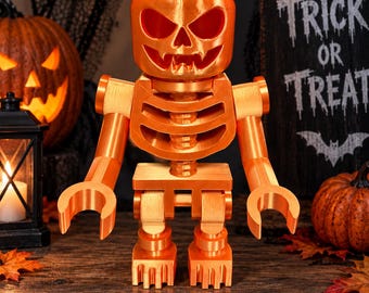 Puede incluir: Una figura de plástico naranja brillante con forma de juguete de bloques, con una cabeza de calabaza tallada que presenta ojos huecos y una boca dentada. El torso se asemeja a una caja torácica y las extremidades tienen articulaciones con manos en C.