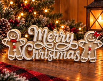 Puede incluir: Un letrero de Merry Christmas en color canela y blanco con dos figuras de pan de jengibre. La figura izquierda lleva pajarita y botones rojos, mientras que la derecha tiene un lazo rojo en el pelo y botones rojos. Texto en fuente cursiva.