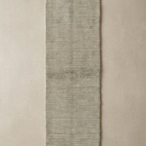 May include: A rectangular, light gray rug with a textured surface. The rug is a neutral color and appears to be made of woven material. The rug is long and narrow, suitable for a hallway or entryway.