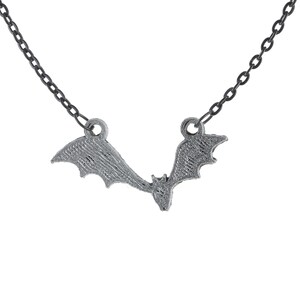 May include: A silver-colored bat pendant necklace. The bat is in flight with outstretched wings, suspended from a dark chain. The necklace is a gothic-themed accessory.