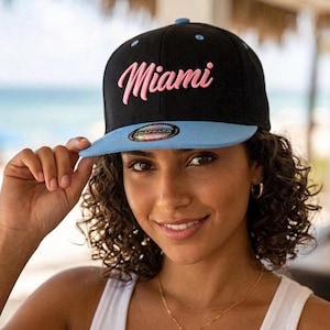 Gorra snapback Miami Pink Script: negra, visera azul, estilo streetwear.