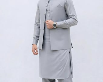 May include: A light gray three-piece suit consisting of a long-sleeved shirt, vest, and loose-fitting pants. The suit has a mandarin collar and a pocket on the vest. The person is wearing a silver watch and black shoes.