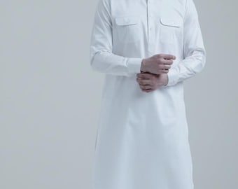 May include: A white, long-sleeved tunic and matching pants set. The tunic has two chest pockets and a button-down front. The outfit is paired with black sandals. The clothing is made of a lightweight fabric.