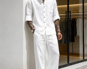 Può includere: Una camicia bianca a maniche lunghe con colletto alla coreana e abbottonatura frontale, abbinata a pantaloni bianchi ampi coordinati con coulisse in vita. La camicia presenta una tasca sul petto e maniche arrotolate fino ai gomiti.