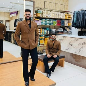 Pode incluir: Um blazer marrom de abotoamento duplo e cal&ccedil;as pretas. O blazer tem um design cl&aacute;ssico. A imagem mostra uma loja de roupas, com um espelho e prateleiras de roupas ao fundo.