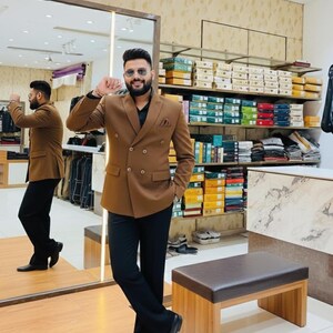 Pode incluir: Um blazer castanho de abotoamento duplo, camisa preta e cal&ccedil;as pretas. O blazer tem duas fileiras de bot&otilde;es e um len&ccedil;o de bolso. A pessoa est&aacute; a usar sapatos pretos. Ao fundo, prateleiras com roupa e acess&oacute;rios.