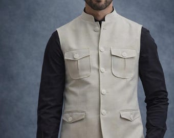 May include: A light beige vest with a mandarin collar and three front pockets. The vest is buttoned up and worn over a black long-sleeve shirt and black pants. The outfit is a formal style.