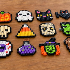 Peut inclure: Un ensemble de douze motifs d'Halloween réalisés en perles à repasser, disposés sur trois rangées. Les figures incluent une citrouille, un fantôme, un chat noir, une chauve-souris, un crâne, un bonbon, une momie, un monstre, un œil, une potion, une sorcière et un cercueil.