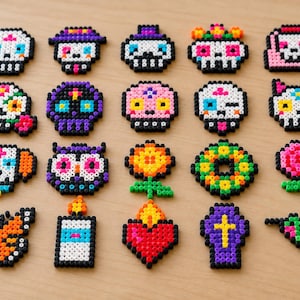 May include: A collection of twenty colorful pixel art figures made from plastic beads, arranged in four rows. The designs include various sugar skulls, a cat, an owl, a dog, a butterfly, a candle, a heart, a coffin, and a hummingbird.