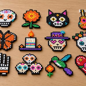 May include: A collection of twelve pixel art figures made from colorful plastic beads. The set includes skulls, a flower, a cat, a guitar, a butterfly, a candle, a hat-wearing skull, a hummingbird, a hand, and a heart shape.