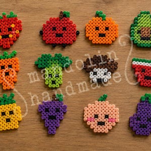 May include: A collection of eleven fruit and vegetable figures crafted from colorful plastic fuse beads. Each piece features a simple, pixelated design with a small face, including a strawberry, apple, orange, avocado, carrot, broccoli, mushroom, watermelon, pineapple, grapes, peach, and eggplant.