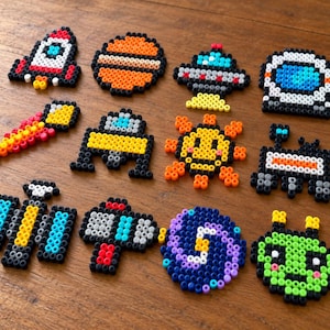 May include: A collection of twelve space-themed fuse bead designs including a rocket, a planet, a UFO, an astronaut helmet, a shooting star, a satellite, a sun, a rover, a space station, a ray gun, a galaxy, and a green alien head.