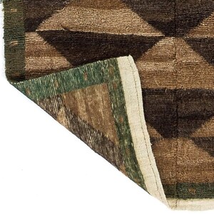 May include: Close-up of a brown and green geometric patterned rug. The rug features a diamond pattern in shades of brown and green, with a cream-colored border. The rug's texture appears to be woven.
