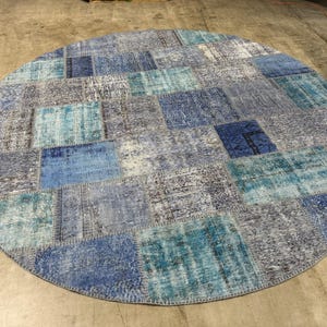 May include: A large circular area rug featuring a patchwork design composed of various rectangular segments in shades of blue, turquoise, grey, and white. The rug displays a distressed, weathered texture with visible stitching between each fabric piece.