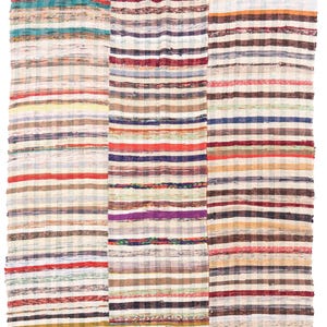 May include: A rectangular woven rug featuring a multi-colored striped pattern across three distinct vertical sections. The fabric displays horizontal bands in shades of red, blue, yellow, green, purple, and brown, interspersed with cream-colored textured weave.