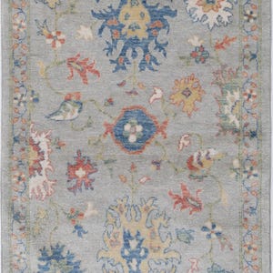 May include: A rectangular, gray rug with a floral pattern. The rug features a central design of blue and yellow flowers, surrounded by red, white, and blue floral accents. The border has a repeating floral pattern.