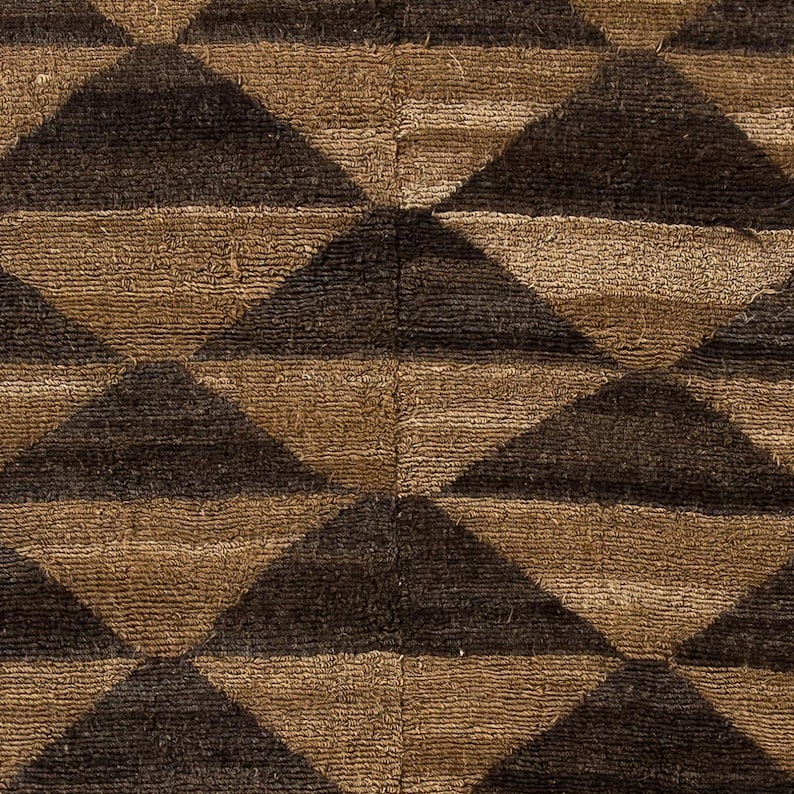 May include: Close-up of a textured fabric with a repeating geometric pattern. The design features alternating rows of brown and dark brown triangles, creating a bold, graphic effect. The fabric appears to be woven or tufted.