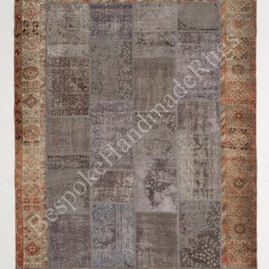 May include: A rectangular patchwork rug featuring a central field of various grey and charcoal fabric segments with faded patterns, surrounded by a wide border in shades of orange, tan, and brown with floral motifs. The text BespokeHandmadeRugs is visible.