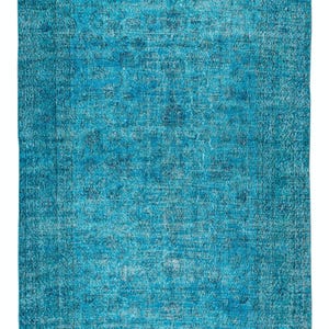 May include: A rectangular, distressed-look rug in shades of turquoise and blue. The rug has a faded, vintage appearance with a central design and a darker border. The texture appears soft and inviting, suitable for a living space.